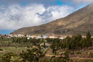 naturskön se av en små by inbäddat i de foten av en berg under en molnig himmel berg landskap med blå himmel och moln i teneriffa. foto