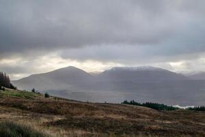 dimmig berg landskap med mulen himmel och rullande kullar i de förgrund i Skottland. foto
