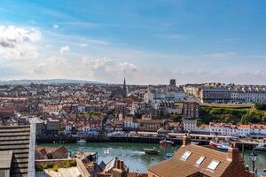 antenn se av en kust stad med historisk byggnader och en hamn under en blå himmel med moln i whitby, england. foto