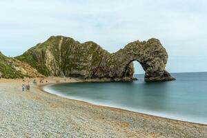 naturskön se av en naturlig båge på en sten strand med lugna hav och molnig himmel på durdle dörr, england. foto