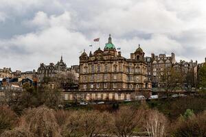 historisk byggnad med koppar kupoler mitt i träd under en molnig himmel, edinburgh. foto