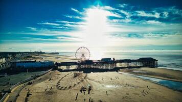 antenn se av en solig strand med en ferris hjul och pir, med människor njuter de havet i backpool, england. foto