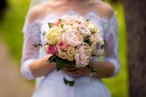 brud i en klänning stående i en grön trädgård och innehav en bröllop bukett av blommor och grönska foto