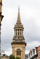 historisk sten kyrka spira mot molnig himmel, med omgivande byggnader i oxford, england. foto