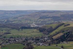 antenn se av en pittoresk by inbäddat i en frodig dal med rullande kullar och en framträdande fabrik i de bakgrund i topp distrikt, england. foto