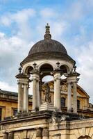 klassisk europeisk arkitektur terar en sten kupol med kolonner och en staty under en molnig himmel i oxford, england. foto