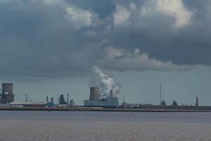 industriell landskap med skorstenar emitterande rök över en kropp av vatten under en molnig himmel. foto