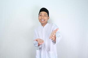 attraktiv muslim asiatisk man presenter hand framåt- på kamera med leende ansikte isolerat på vit bakgrund, ser på kamera foto