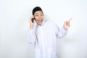 Lycklig muslim asiatisk man utseende överraskad medan talande på de telefon med pekande hand foto