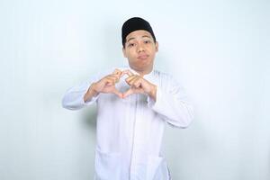 olycklig asiatisk muslim man ser på kamera och visa hjärta form isolerat på vit bakgrund foto