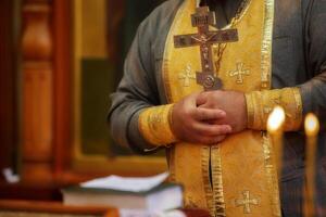 de prästens händer håll en korsa mot en bakgrund av flimmer ljus. religion och tro. foto
