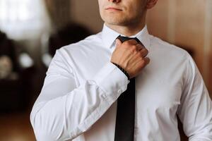 man i skjorta klä på sig upp och justeras slips på nacke på Hem. bröllop dag koncept, mode, företag, manlig stil. foto