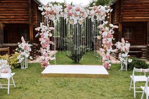 gyllene båge dekorerad med blommor på de bakgrund av träd. en vit väg den där leder till de båge, många vit stolar. förberedelse för de bröllop ceremoni foto