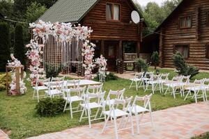 gyllene båge dekorerad med blommor på de bakgrund av träd. en vit väg den där leder till de båge, många vit stolar. förberedelse för de bröllop ceremoni foto