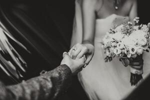 brudgum hjälper Lycklig ung brud till skaffa sig ut av bröllop bil. svart och vit Foto