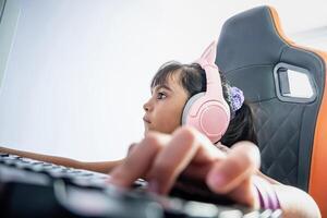 latin liten flicka banderoll spelar. hon är koncentrerad spelar uppkopplad spel. hon är bär hörlurar och Sammanträde i en gaming stol. foto