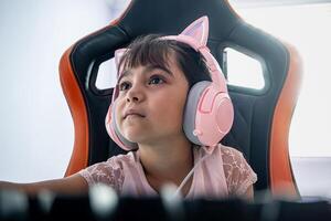 förtjusande gamer flicka spelar på de dator i de sovrum. hon är en liten flicka bär skön hörlurar med katt öron. foto