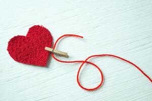 plysch hjärta fångad förbi en klädnypa med en röd tråd på en vit trä- tabell. foto