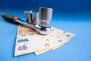 begrepp av de kosta av mekanik tillverkad med en spärr rycka och argentine peso räkningar på en blå bakgrund. foto