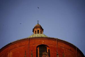 fåglar cirkel de kupol av ett italiensk terrakotta kyrka i de miljö Sol foto