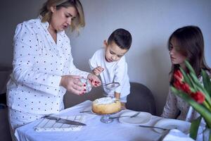 familj av tre, mor, Tonårs dotter och liten son, äter kaka i pyjamas på en tabell med tulpaner foto