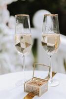 formad champagne glasögon och en glas låda med guld bröllop ringar i de mitten. förberedelse för de bröllop ceremoni. foto