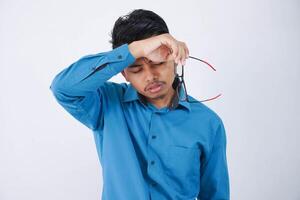 porträtt av utmattad stilig ung asiatisk affärsman i bär blå skjorta tar av glasögon känner trött efter arbetssätt på dator isolerat på vit bakgrund foto