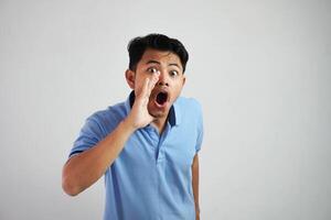 porträtt av en ung asiatisk man skrikande ut högt med hand på hans mun bär blå t skjorta isolerat över vit bakgrund foto