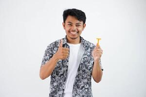 leende eller Lycklig ung asiatisk man innehav rakapparat med tumme upp finger gest isolerat på vit bakgrund foto