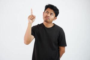förvånad ung asiatisk man bär svart t skjorta stående punkt finger upp isolerat på vit bakgrund foto