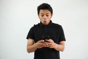 överraskad eller chockade ung asiatisk man isolerat på vit bakgrund innehav telefon och sändning en meddelande foto