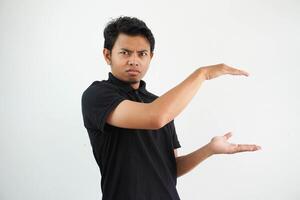 ung asiatisk man Framställ på en vit bakgrund chockade och förvånad innehav en kopia Plats mellan händer, bär svart polo t skjorta. foto