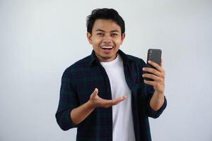 ung asiatisk man ser till kamera som visar Wow uttryck medan innehav mobiltelefon isolerat på vit bakgrund foto
