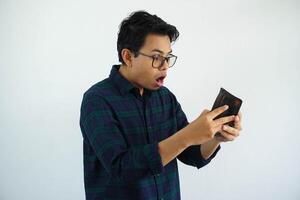 ung asiatisk man som visar chockade ansikte uttryck medan ser till hans plånbok isolerat på vit bakgrund foto