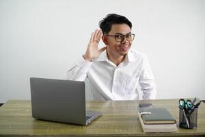 ung asiatisk affärsman i en arbetsplats lyssnande till något förbi sätta hand på de öra bär vit skjorta isolerat på vit bakgrund foto