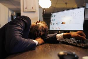 utmattad trött affärsman lidande från sömnighet efter arbetssätt över tid på projekt i börja kontor. dränerad afrikansk amerikan anställd med burnout syndrom sovande på arbete. företag begrepp foto