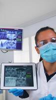 patient pOV i dental kontor diskuterar behandling av tänder hålighet, tandläkare pekande på digital röntgen använder sig av läsplatta. team av doktorer arbetssätt i modern stomatologisk klinik, förklara radiografi tand foto