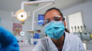 pOV av patient i en dental klinik Sammanträde på kirurgi stol kontroll påverkade massa. tandvård team arbetssätt i ortodontisk kontor, belysning de lampa och granskning person, närbild ansikte i medicinsk mask. foto