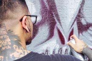 gata graffiti konstnär målning med en Färg spray kan en mörk monster skalle graffiti på de vägg i de stad utomhus- - stänga upp hand målarfärger - urban, livsstil samtida gata konst begrepp foto