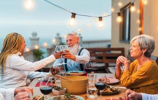 raser senior vänner har roligt dining tillsammans och toasting med röd vin på hus uteplats middag - mat och högtider begrepp foto