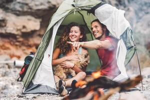 par av trekker Sammanträde i de tält med deras sällskapsdjur - Lycklig man och kvinna har roligt i semester camping runt om sten berg Nästa till de brand - kärlek, resa och relation begrepp foto