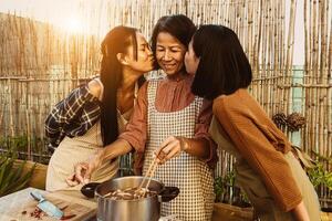 sydöst asiatisk mor med henne döttrar har roligt framställning thai mat recept tillsammans på hus uteplats foto