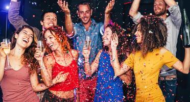 Lycklig vänner håller på med fest dans och dricka champagne på nattklubb - tusenåriga ung människor har roligt fira tillsammans och kasta konfetti - underhållning, ungdom livsstil högtider begrepp foto