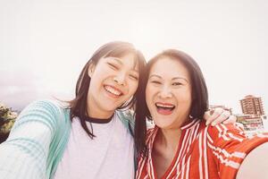 Lycklig mor och dotter tar selfie med mobil smartphone utomhus- - asiatisk familj delning tid och Foto tillsammans - beständighet, kärlek och människor livsstil begrepp