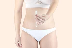 kvinna innehav en menstruation bomull tampong i henne hand, i vit underkläder foto