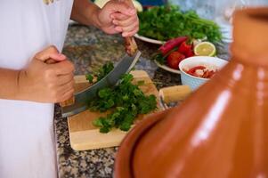 kockens händer hackning persilja och Koriander grön örter för krydda en traditionell marockansk maträtt - grönsaker i tagine foto