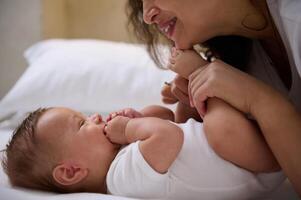 närbild porträtt av en Lycklig ung mor leende till henne härlig bebis pojke, kissing hans mycket liten tår och fötter. barnomsorg foto