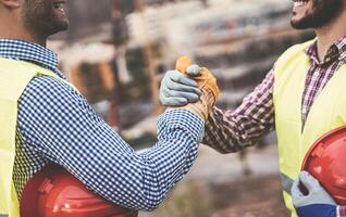 ung byggare skakning händer framställning ett avtal på konstruktion webbplats - arbetare nå en handla och på arbete projekt - byggnad, som handlar om, ingenjör industriell begrepp foto