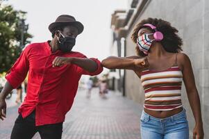 afrikansk vänner bär ansikte skyddande mask medan håller på med ny social distans hälsningar skumpande armbågar - ungdom tusenåriga människor och hälsa vård riktlinjer till undvika korona virus spridning foto