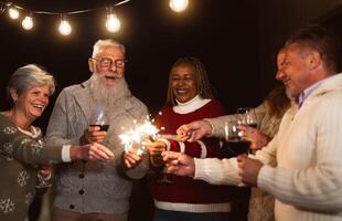 Lycklig seniors har roligt fira högtider dricka vin och innehav sparklers fyrverkeri foto